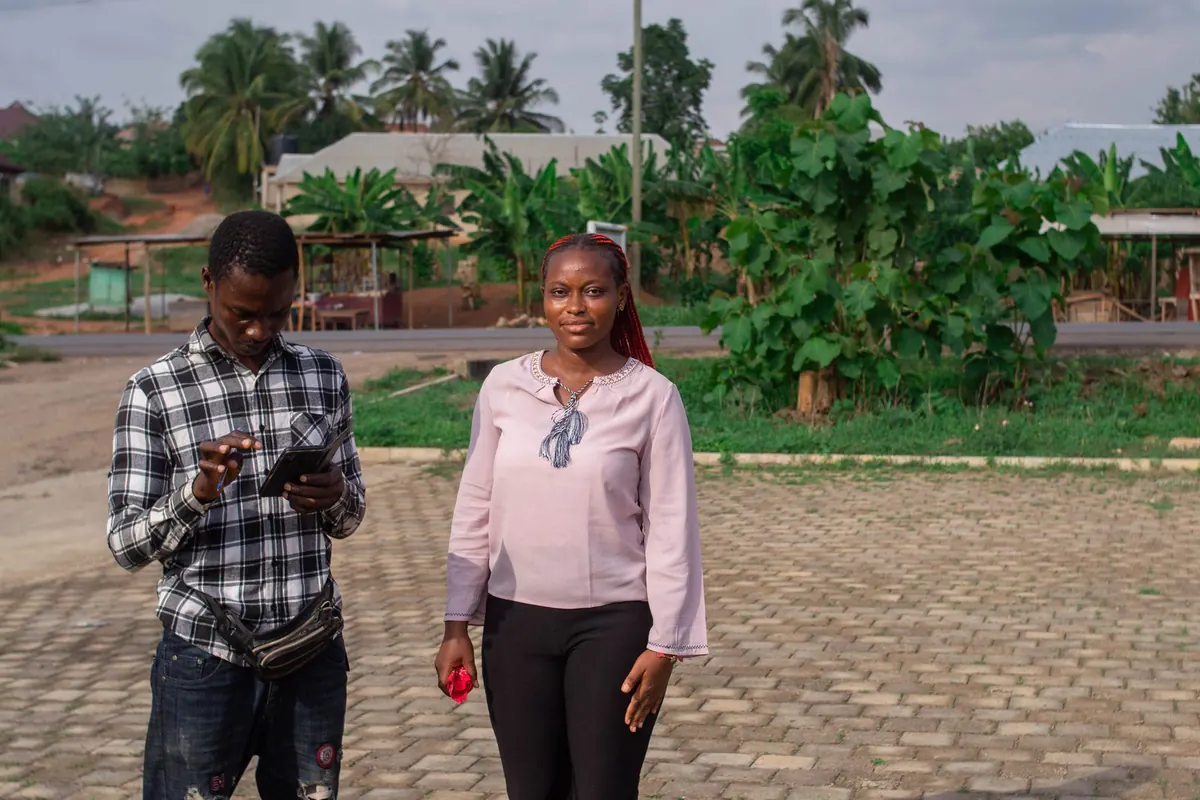 A field researcher reviewing a tablet while walking through a community with a programme participant